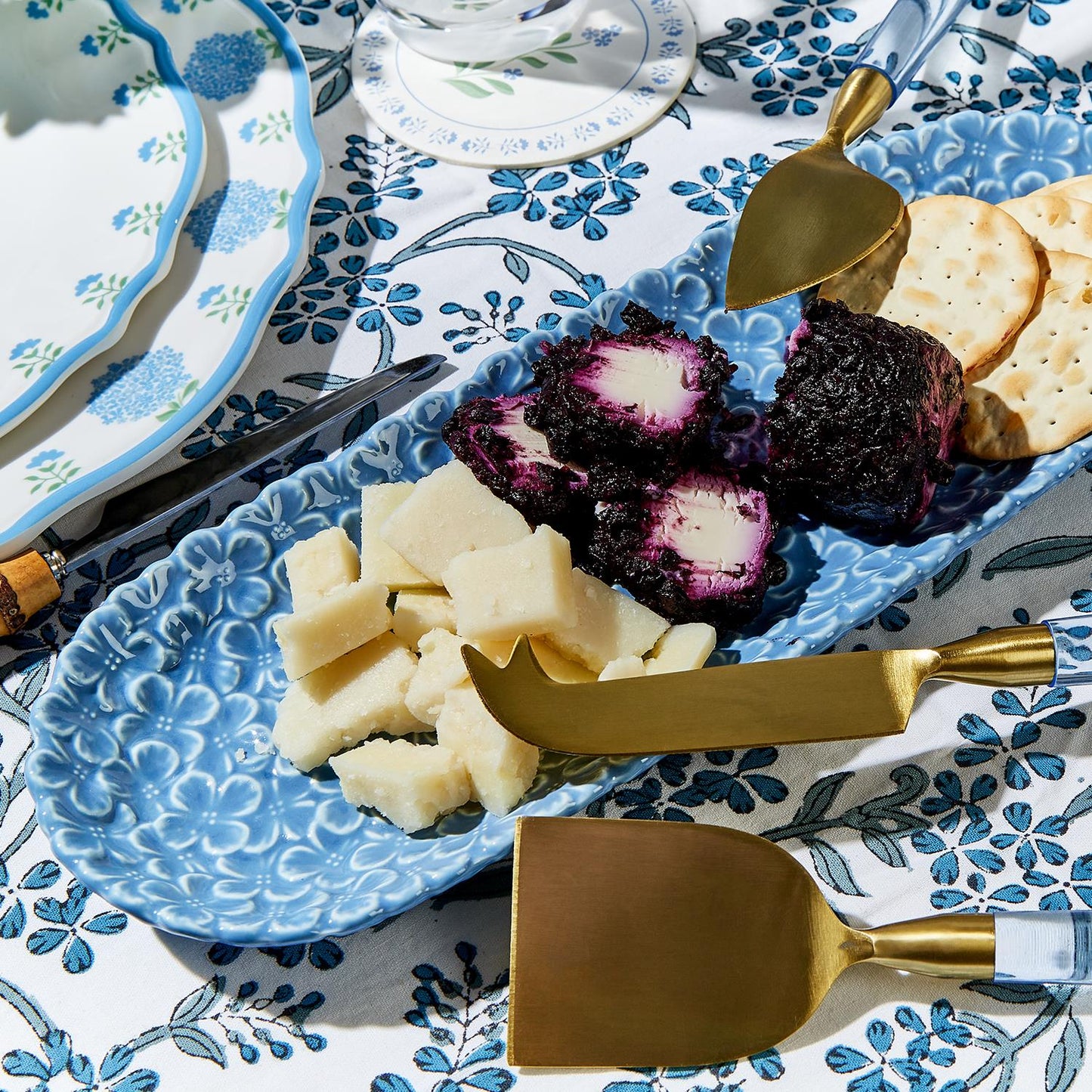 A blue porcelain dish with a floral pattern, containing various food items like cheese and crackers, accompanied by utensils.