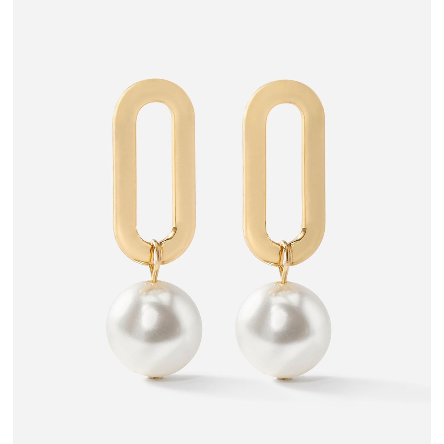 Gold oval droplet earrings with white pearls on a light gray background by Charlie Paige