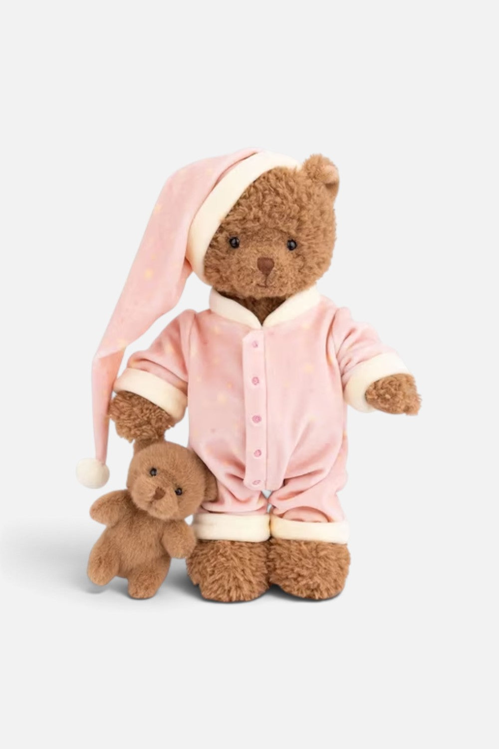 A plush teddy bear wearing a pink velour pajama set with cream trim and a matching sleep hat, posed next to a smaller matching plush bear on a light gray studio background.