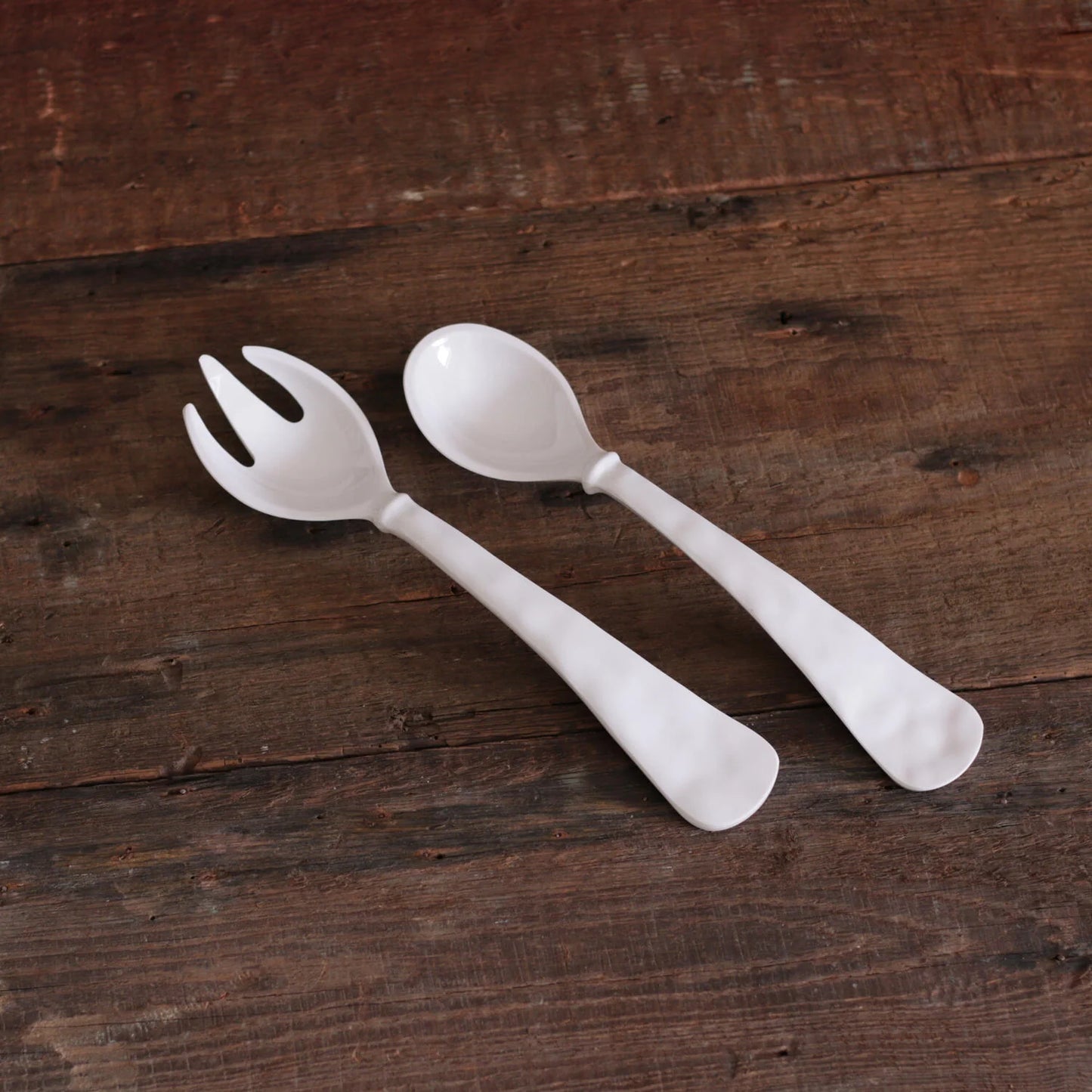 A pair of white melamine salad servers, one with a fork-like end and the other with a spoon-like end.