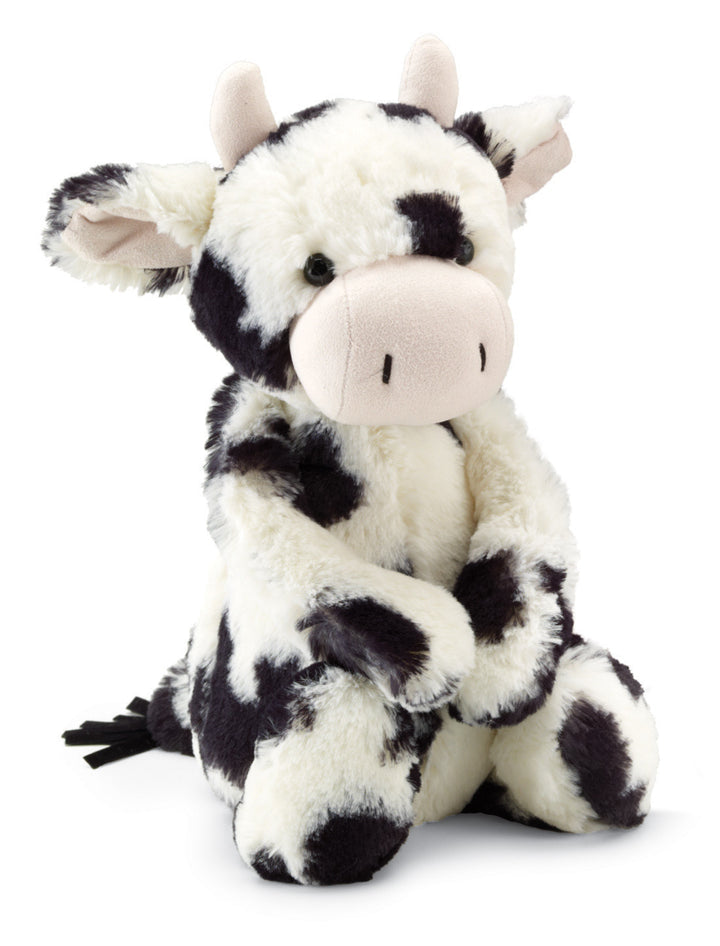 A plush toy resembling a calf with black and white fur patterns, cream-colored hooves, and a pink snout. It has big ears and a swishy tail.