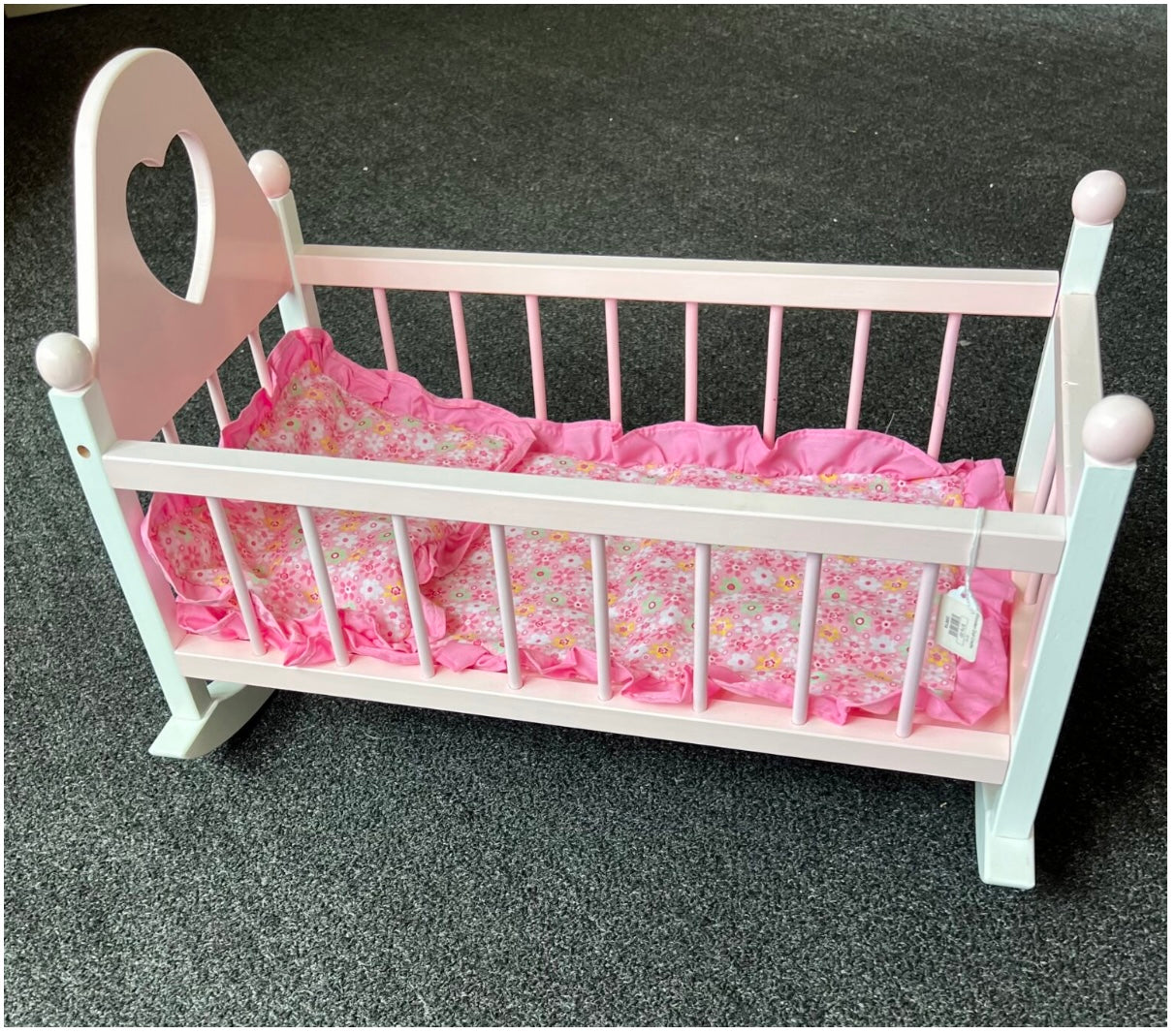 A pink and white wooden rocking cradle with a floral patterned mattress.