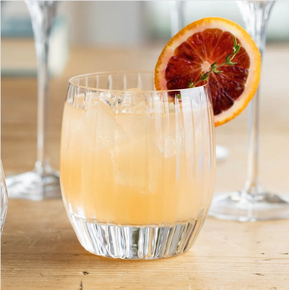 Vietri Double Old Fashioned glass with etched patterns filled with an orange-colored beverage, garnished with a slice of citrus, possibly blood orange, perfect cocktail glass.