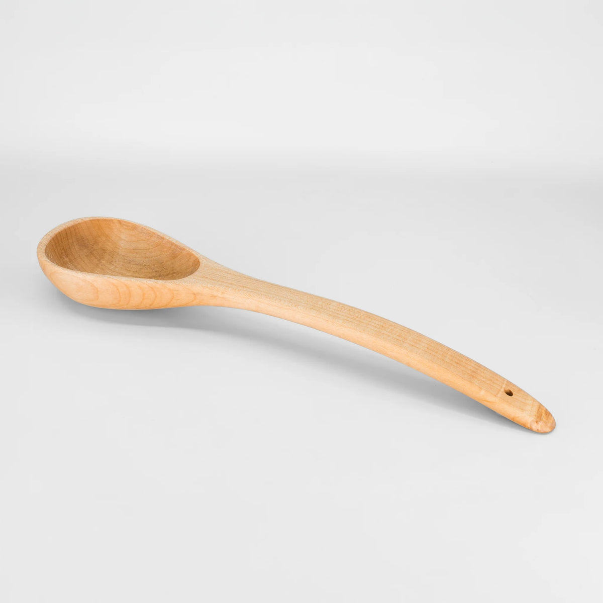 A single wooden spoon with a long handle and a small hole near the end, by holland bowl mill photographed on a clean light gray studio background.
