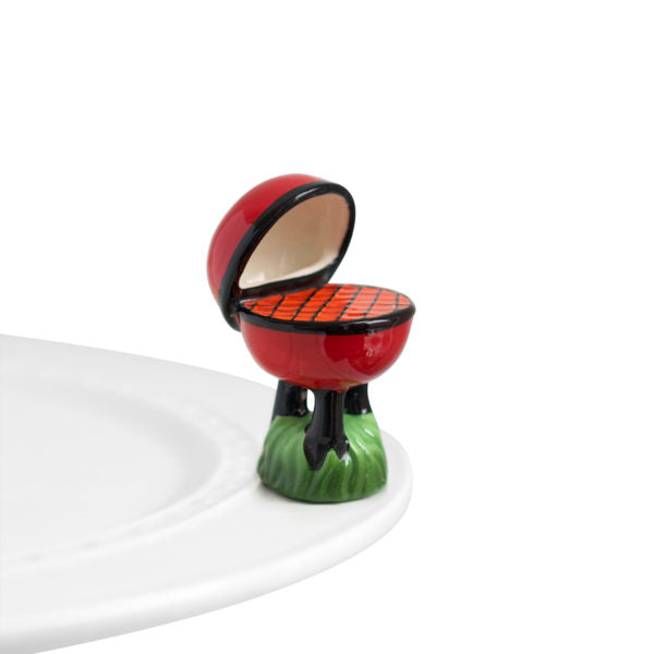 A small, red and green mini figurine of a grill designed to attach to a serving piece.