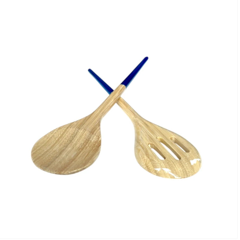 Two wooden salad serving spoons crossed over each other on a plain white background. One spoon has a smooth natural wood finish, and the other has three slots in the bowl, both with blue handles.