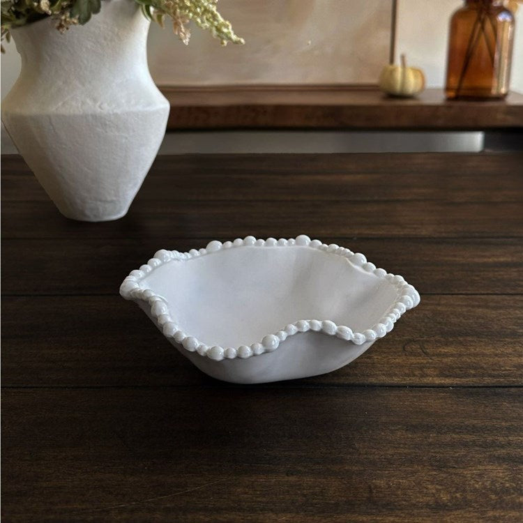 A white, wavy mini bowl with a pearl rim designed by Beatriz Ball, placed on a wooden surface.