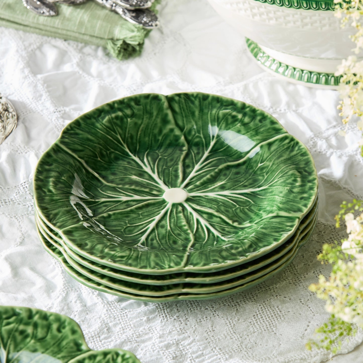Set of green ceramic plates with leaf design on a white lace tablecloth.