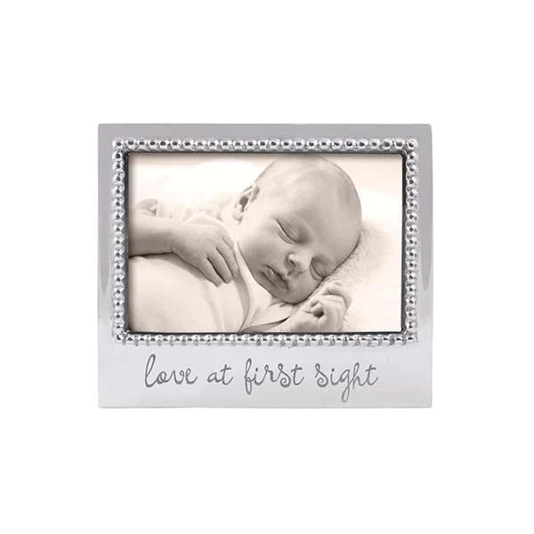 A 4x6 photo frame with a beaded border and 'love at first sight' text, containing a black and white photo of a sleeping baby.