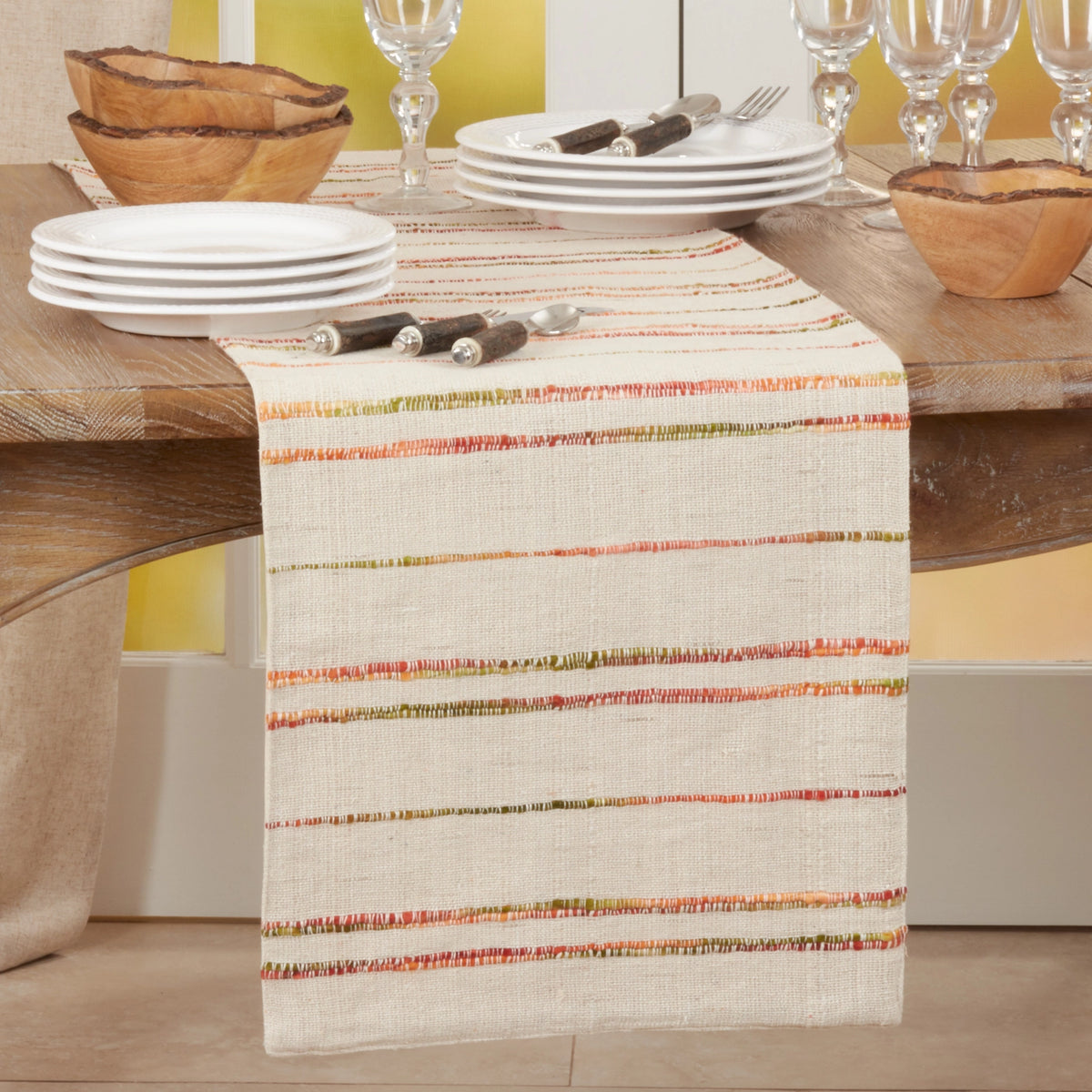 Striped table runner with stripes in shades of green and orange on a beige fabric.