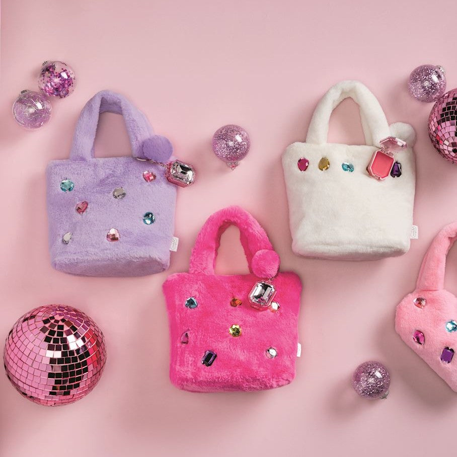 Three plush mini handbags in lavender, hot pink, and white, decorated with faux rhinestones and pom-poms, arranged on a pink background with disco ball props.