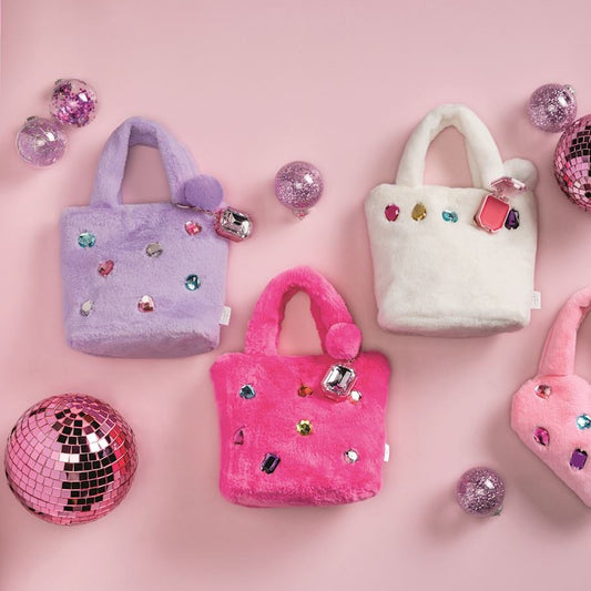 Three plush mini handbags in lavender, hot pink, and white, decorated with faux rhinestones and pom-poms, arranged on a pink background with disco ball props.