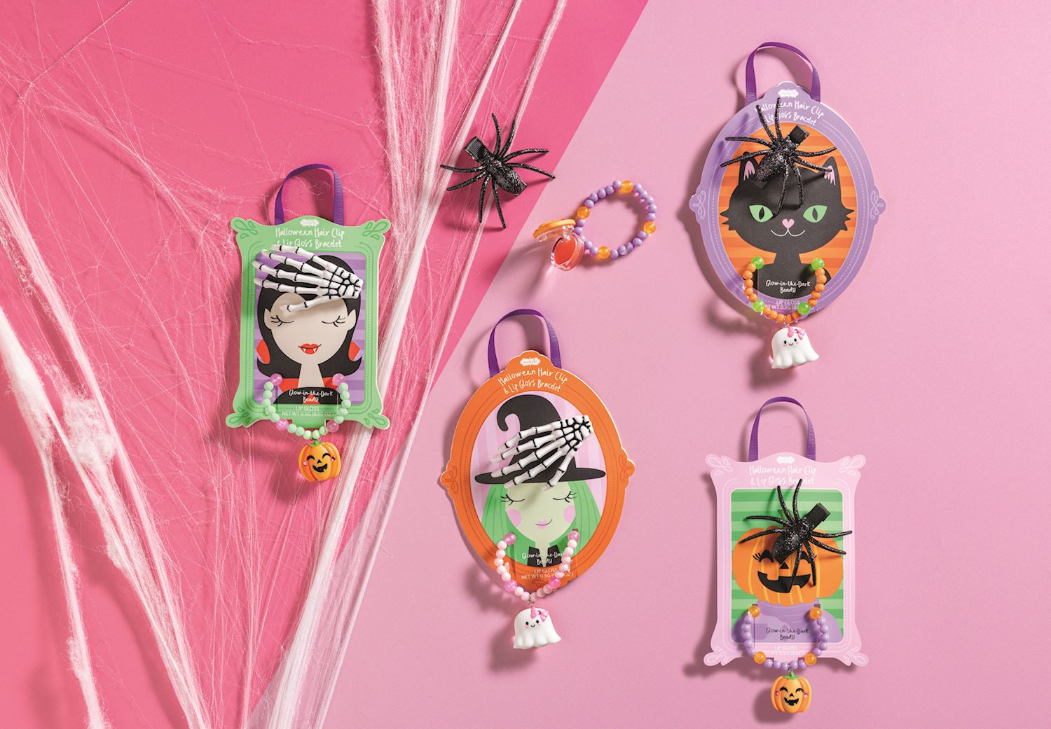 Four Halloween-themed hair clips arranged on a pink background with decorative web and dried grass. The clips feature cartoon illustrations including a vampire, a black cat in a mirror frame, a witch, and a jack-o'-lantern on pastel backgrounds.