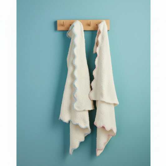 Two white towels with ruffled edges of blue and pink hanging on a wooden towel rack against a blue wall.