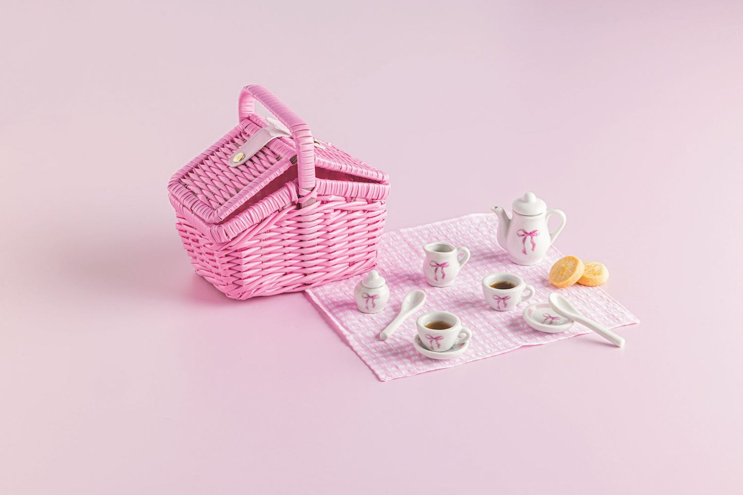 Pink wicker picnic basket with tea set on a pink background