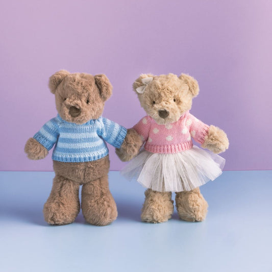 Two teddy bears, one in a sweater and the other in a dress, standing against a purple background.