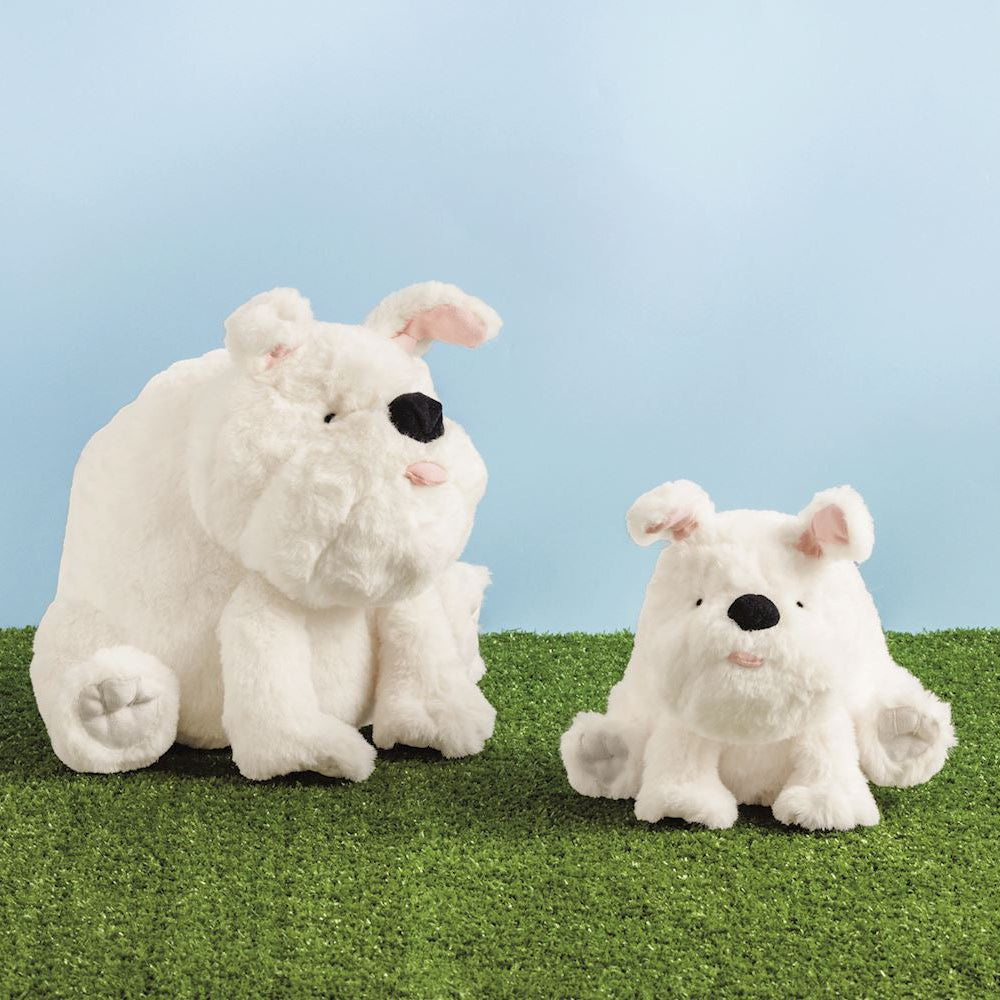 Two white plush bulldog toys, one larger and one smaller, sitting on green artificial grass against a light blue background.
