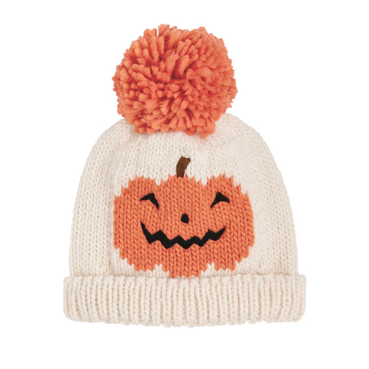 An off-white knit beanie hat featuring a knitted orange jack-o'-lantern face on the front and a matching orange pom-pom on top