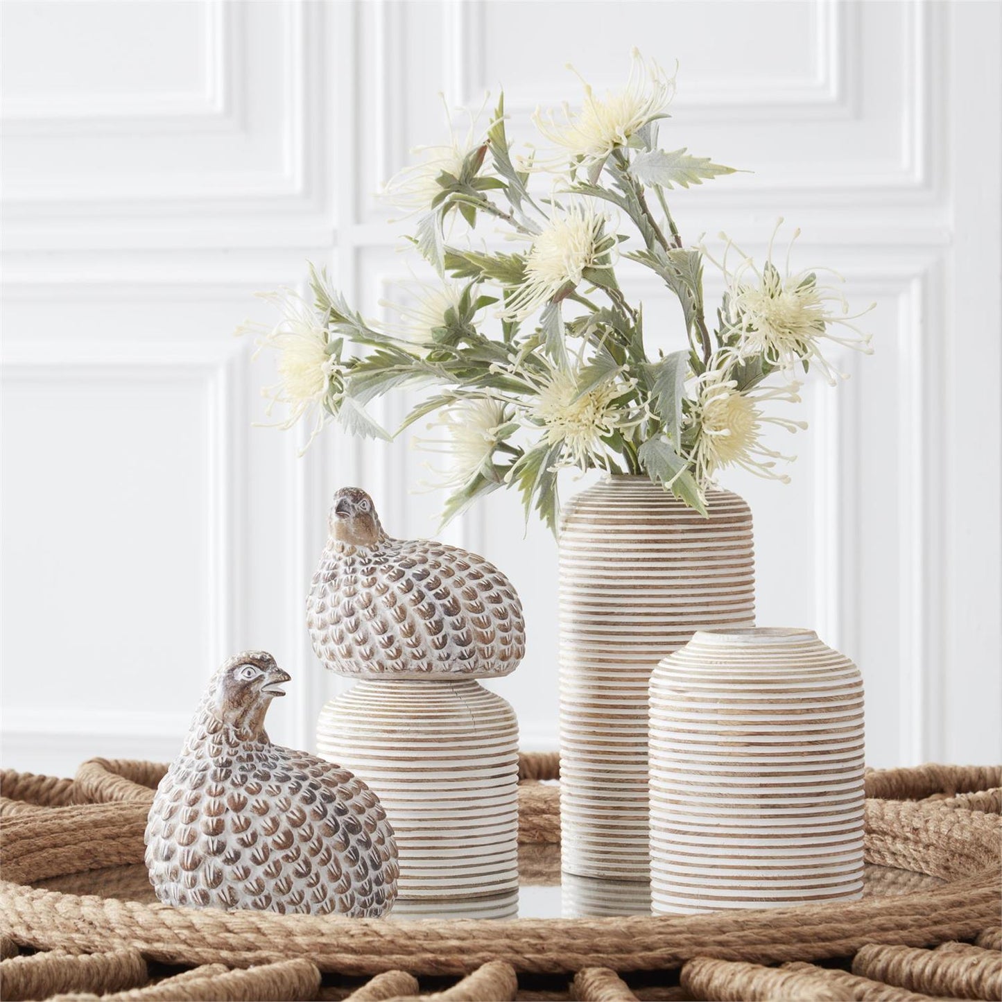 Set of decorative vases and quail figurines on a textured surface with a white paneled wall in the background.