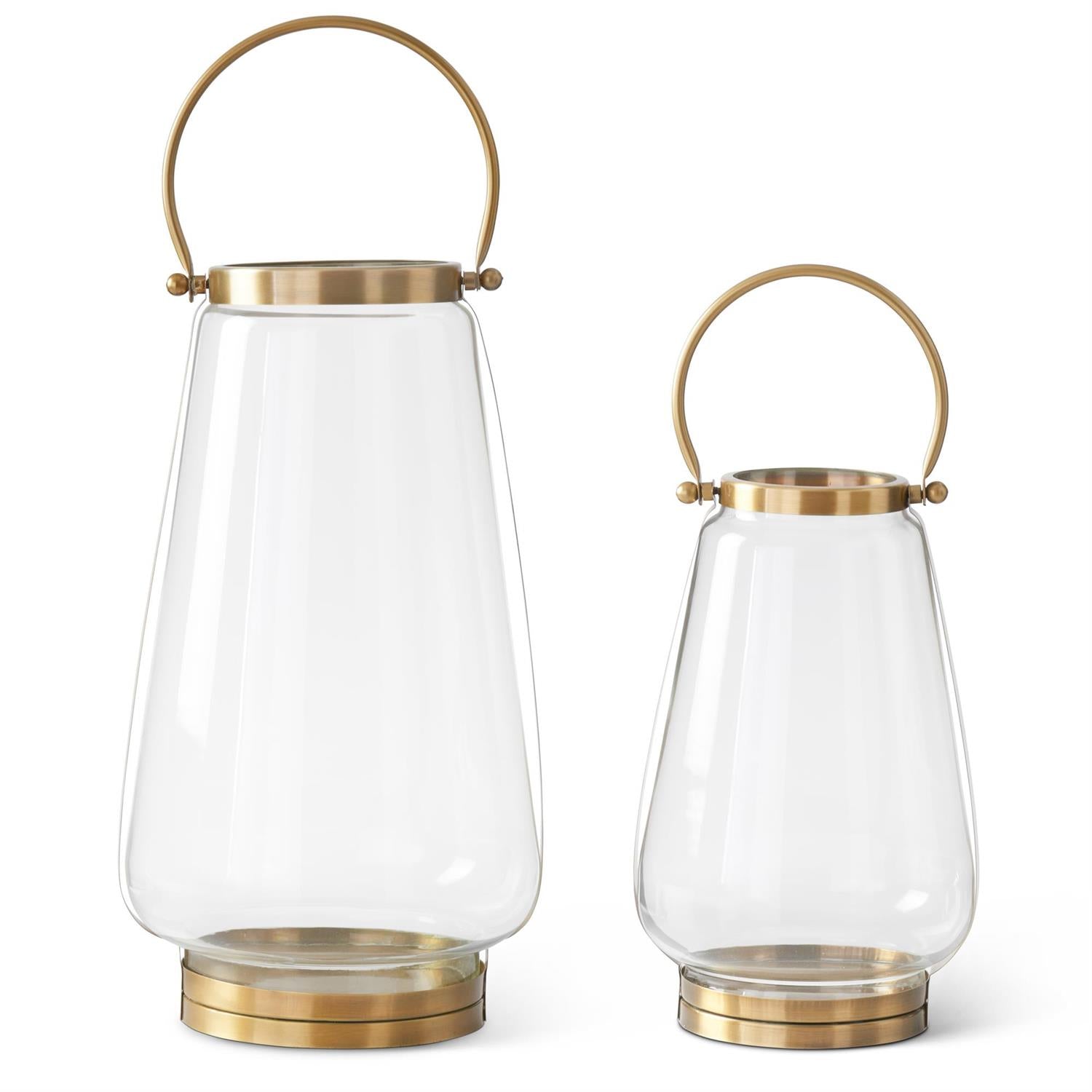 Two clear glass lanterns with gold metal accents and a gold handle on a white background
