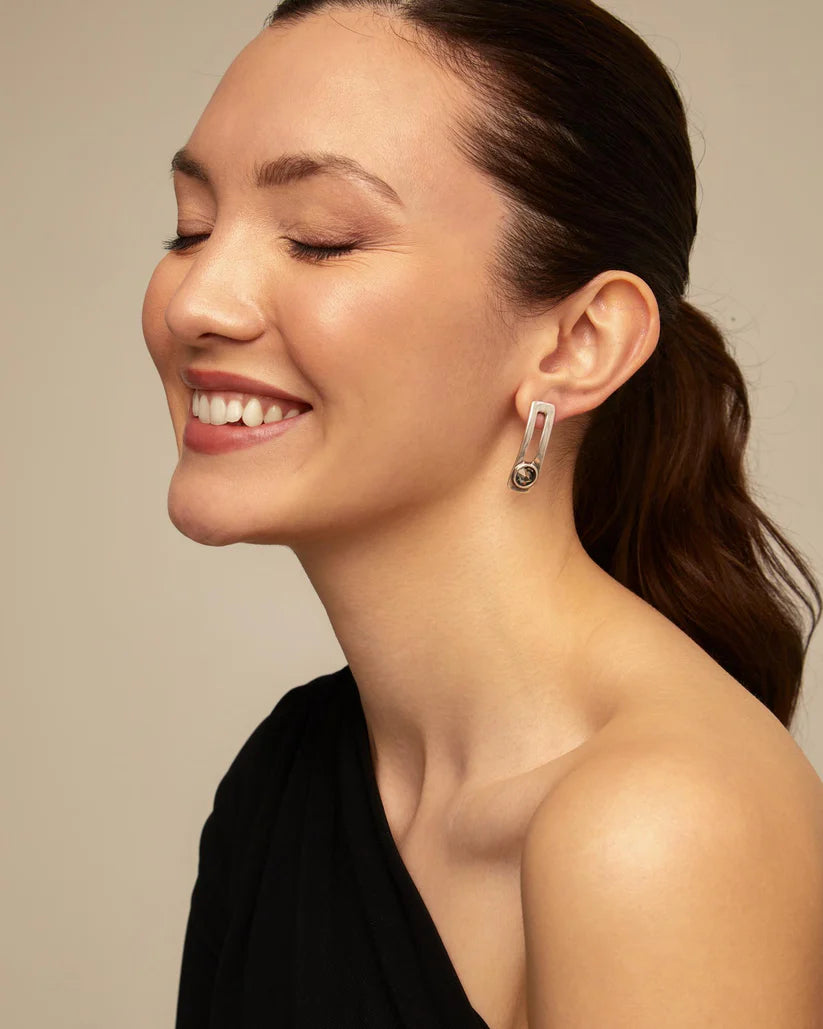 Woman wearing a silver UNOde50 On my own earring with a dark stone against a neutral background