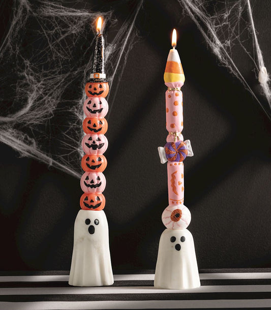 Halloween-themed candles with ghost bases on a dark background with spider webs.