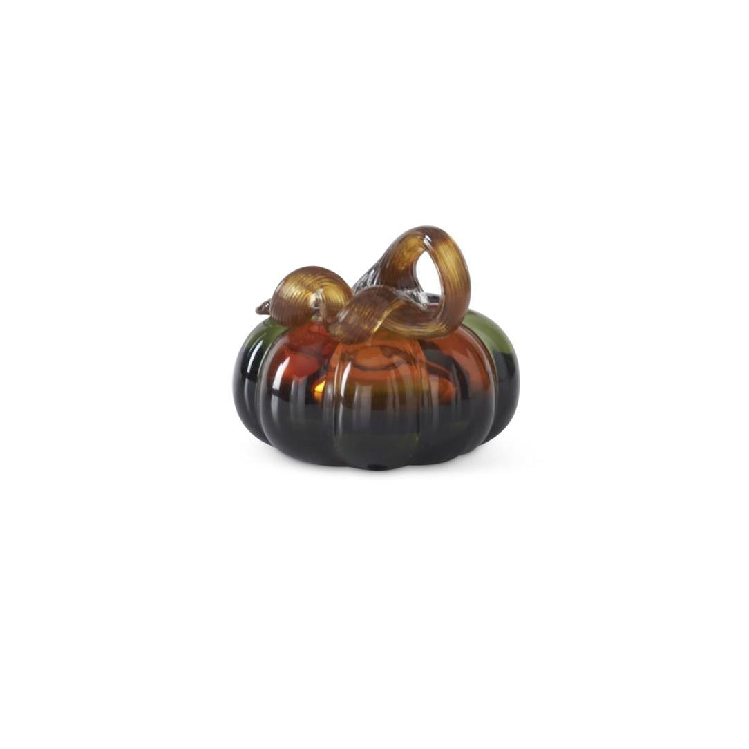 A small hand-blown glass pumpkin with a twisted stem featuring amber, brown, and dark green tones, set against a plain white background.