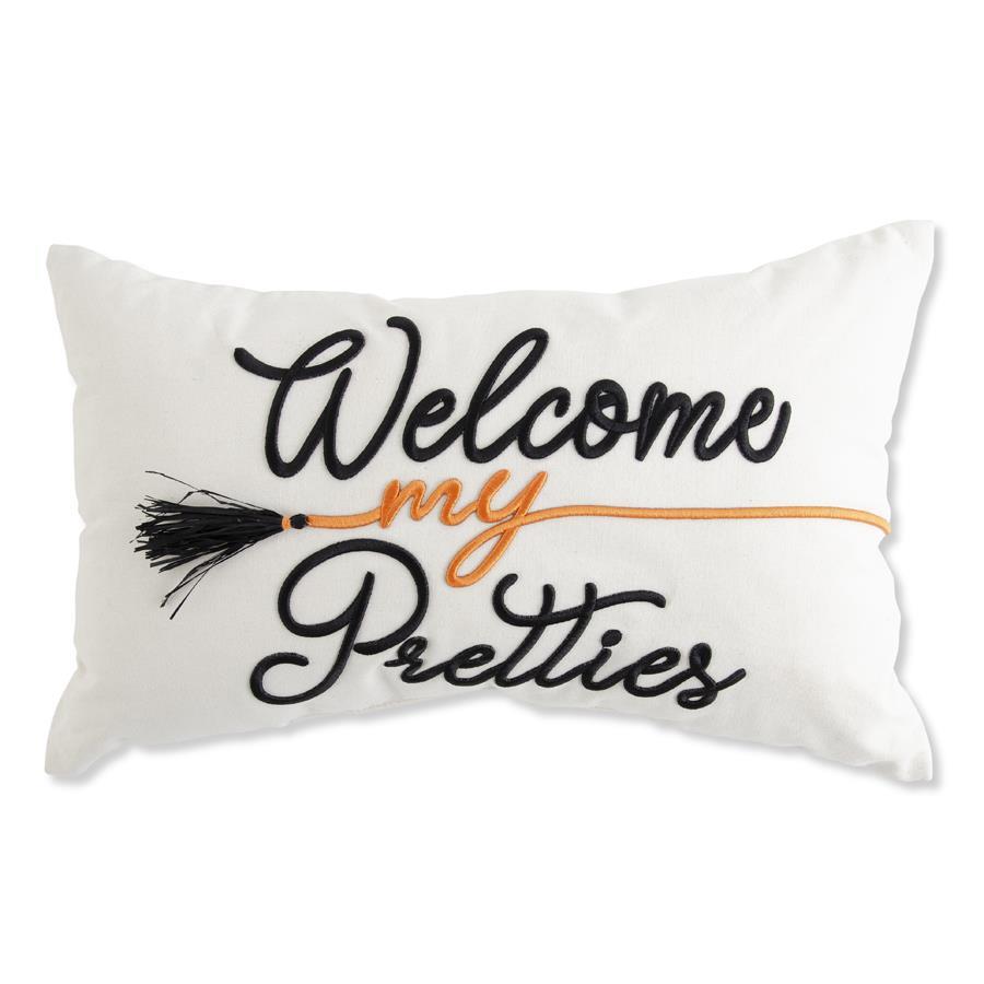 A rectangular white throw pillow featuring embroidered text that reads 'Welcome my Pretties' in black and orange, with a black broom tassel detail, shown against a plain white background.
