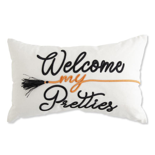 A rectangular white throw pillow featuring embroidered text that reads 'Welcome my Pretties' in black and orange, with a black broom tassel detail, shown against a plain white background.