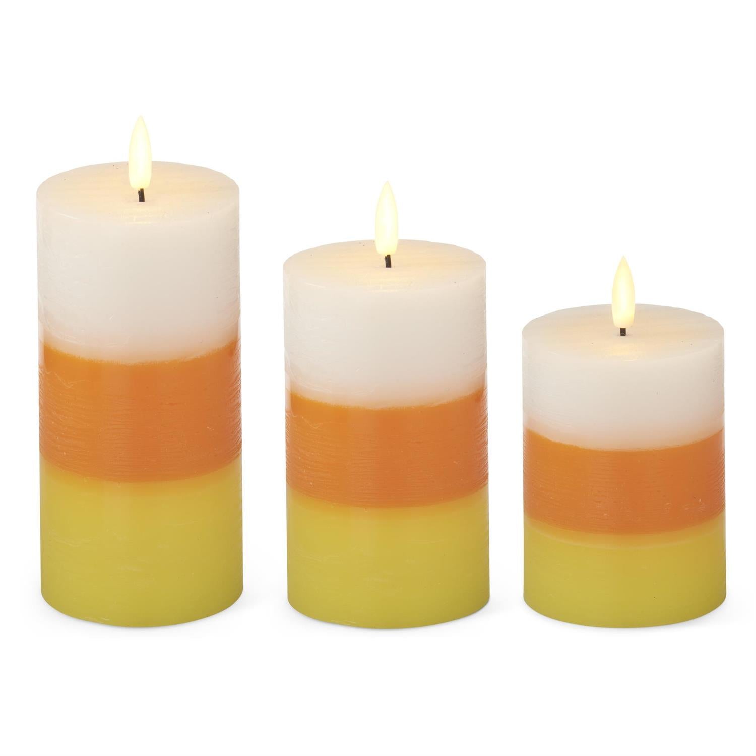 Three flameless pillar candles in graduated sizes with horizontal candy corn stripes in white, orange, and yellow on a plain white background.