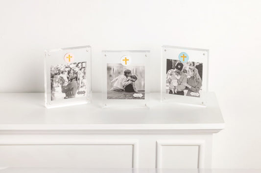 Three photo frames by mudpie with a colored circle and a gold cross with family pictures on a white surface