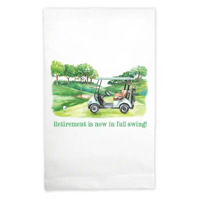 Tea towel with a golf cart on a golf course and text 'Retirement is now in full swing!' on a white background.