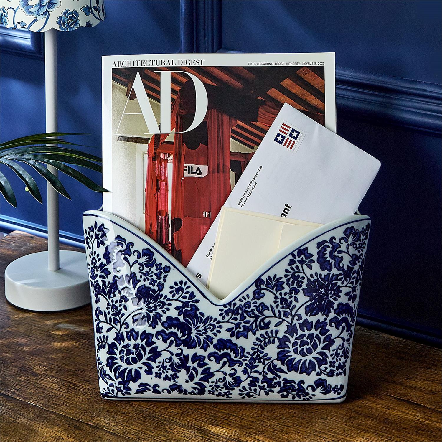 Decorative blue and white letter holder with mail and a magazine on a wooden surface.