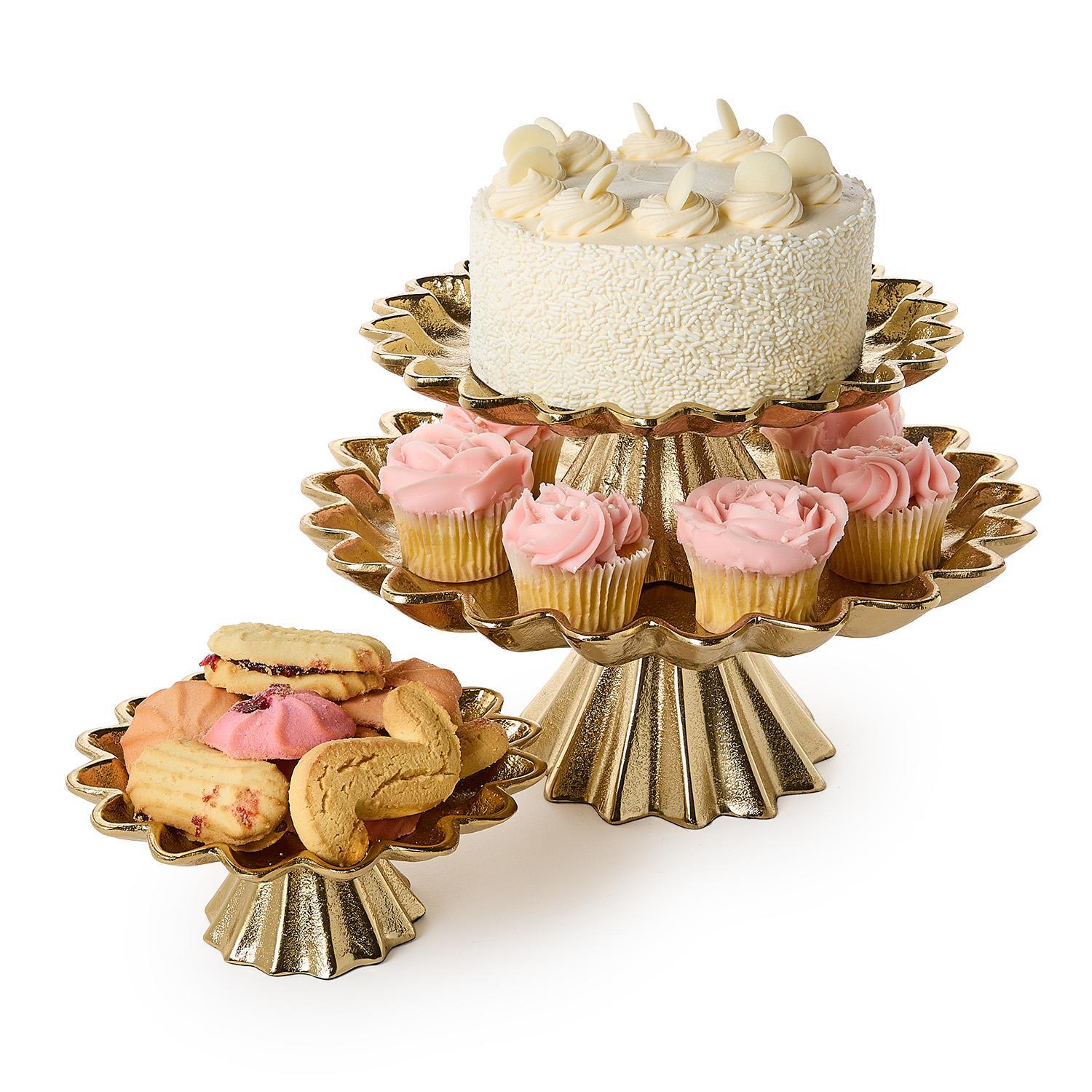 Gold cake stand with a cake and cupcakes on a white background
