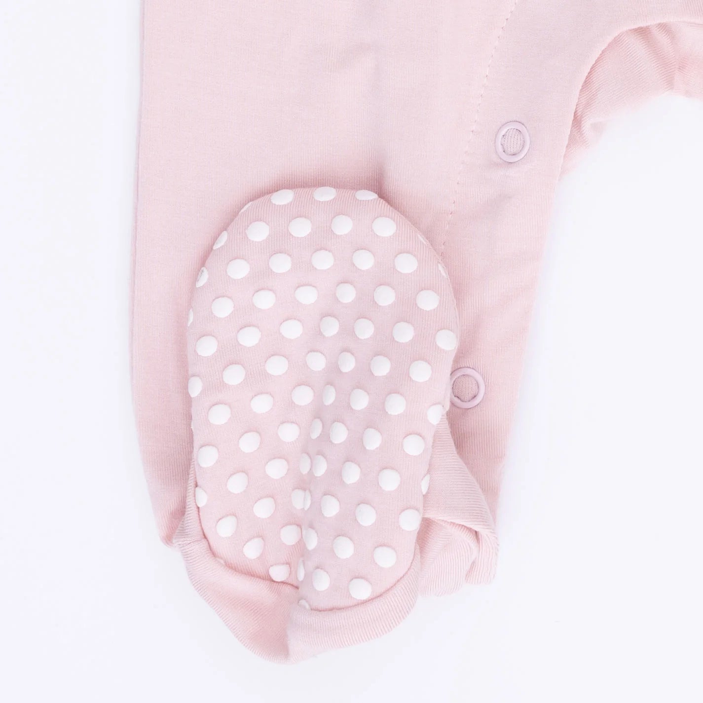 Rubber dotted foot on an Angel Dear Dainty Buds & Bows Footie Pink baby onesie with white floral and bow print top, light pink bottoms with a pink bow  on a white background