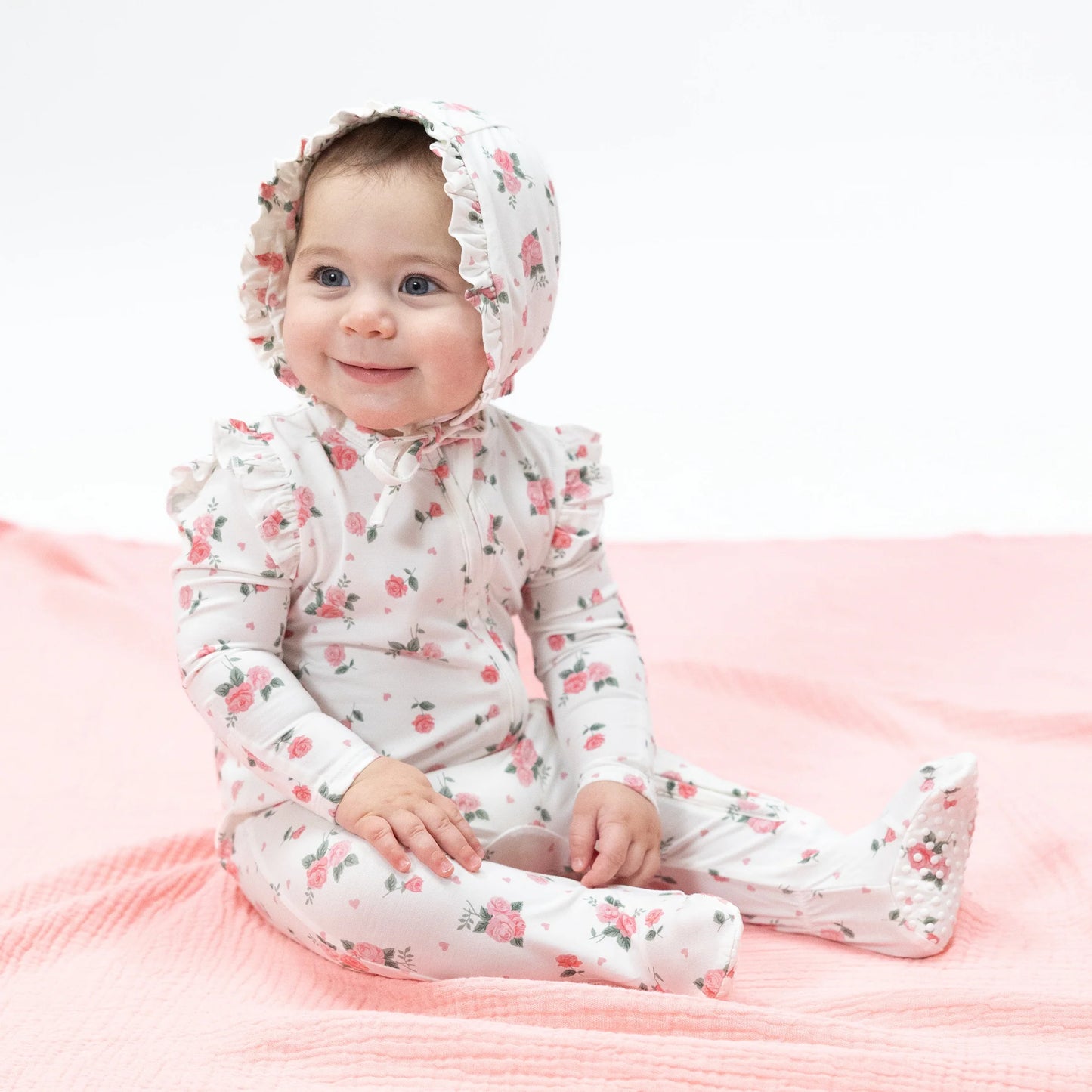 Baby wearing Angel Dear Pink Rosettes 2 Way Ruffle Sleeve Zipper Footie with a matching bonnet
