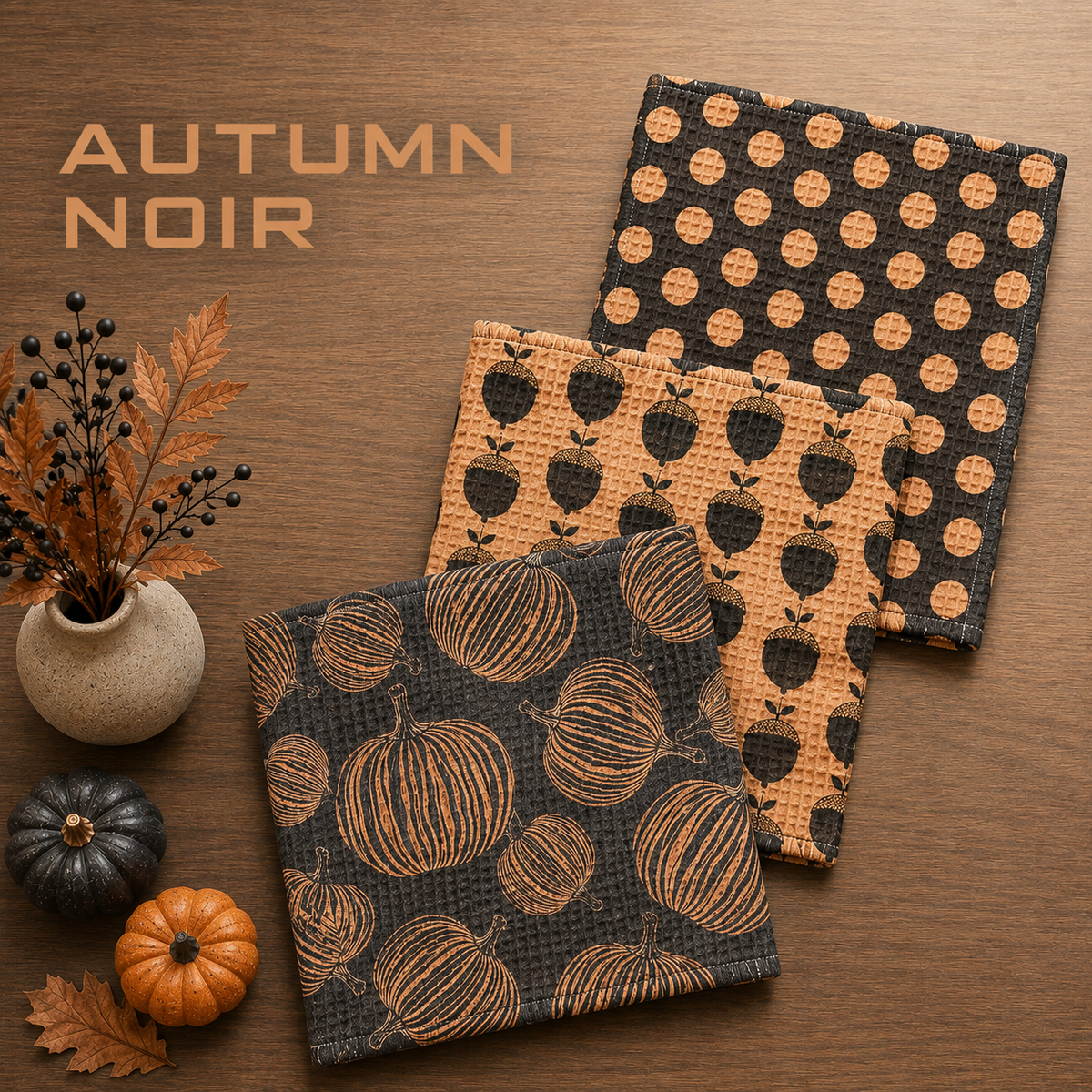 Geometry Autumn Noir Dishcloth set with Three textured fabric square cloths with autumn patterns are arranged on a wooden surface. The cloths feature black and orange pumpkin, apple, and polka dot designs.  The Little Exchange SKU 150099