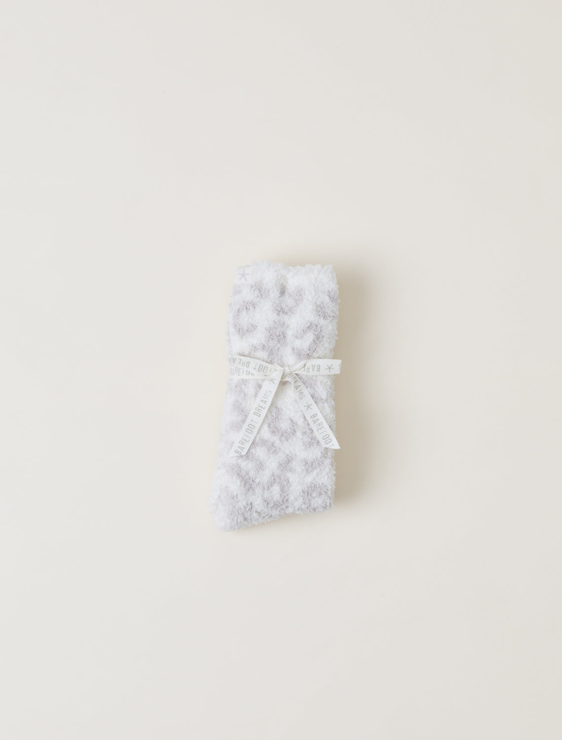barefoot dreams cozy chic leopard print socks in a light gray pattern, tied with a white ribbon, on a solid off-white background.