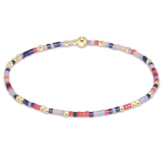 A delicate beaded bracelet with alternating segments of navy blue, light blue, pink, and red beads, accented by small gold spacer beads and a central gold sphere clasp, shown on a plain white background.