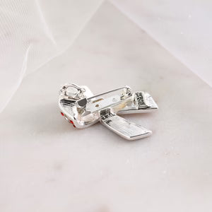 Back of a patriotic brooche silver-toned metal charm shaped like a ribbon bow with a small hanging loop, photographed on a soft white surface with a sheer white fabric backdrop.