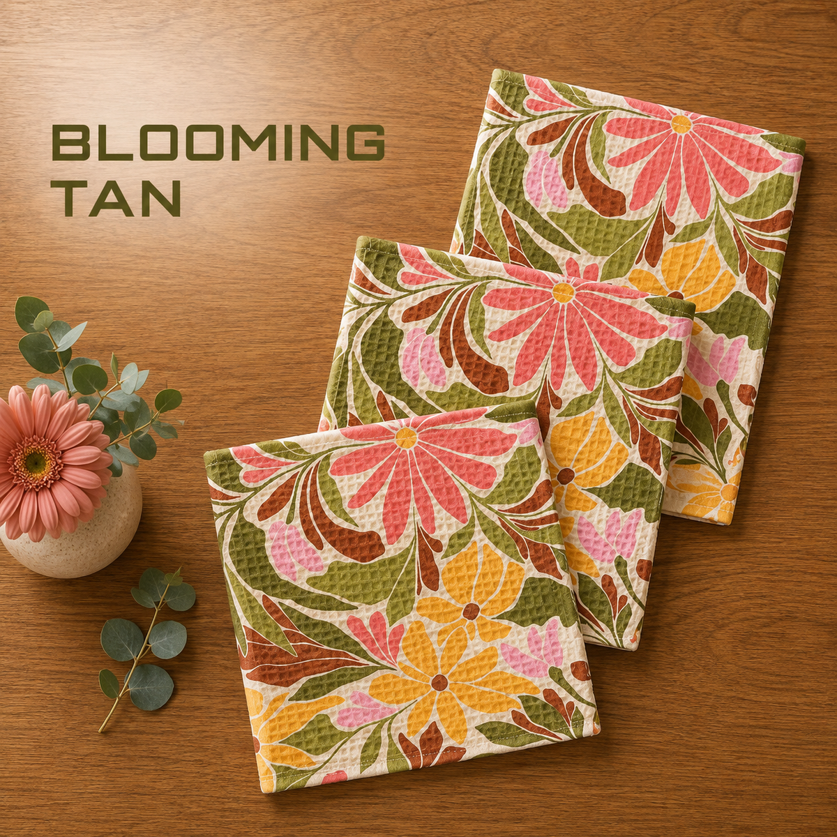 Geometry Blooming tan dishcloth set with Three disclothes with a retro floral pattern in pink, yellow, green, and brown, arranged on a wooden table next to a small pink flower and eucalyptus sprig. The text 'BLOOMING TAN' is displayed in the upper left corner.  The Little Exchange SKU 148282