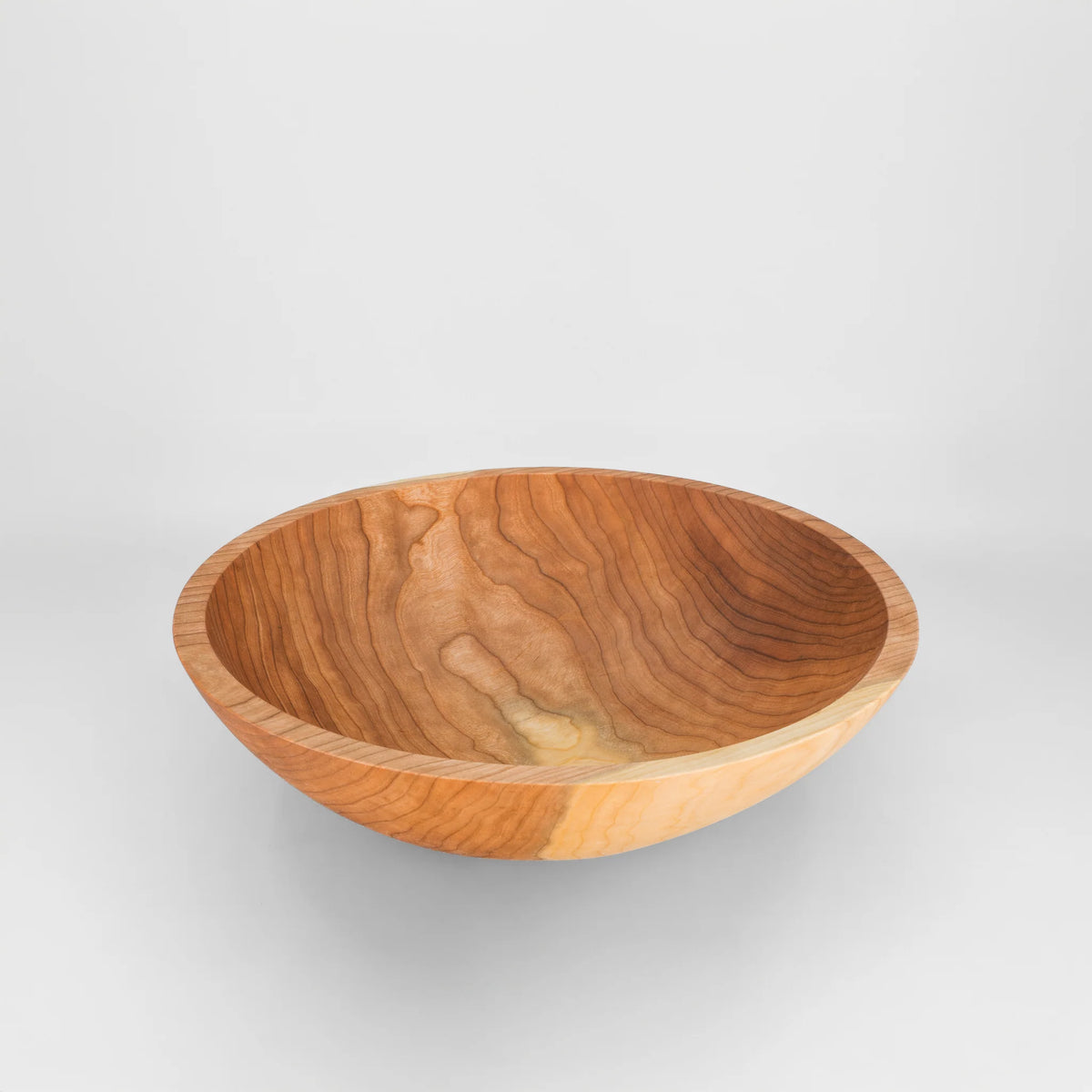 A handcrafted cherry wooden bowl with a rich grain pattern, from holland bowl mill shown from a direct overhead angle on a light gray background.