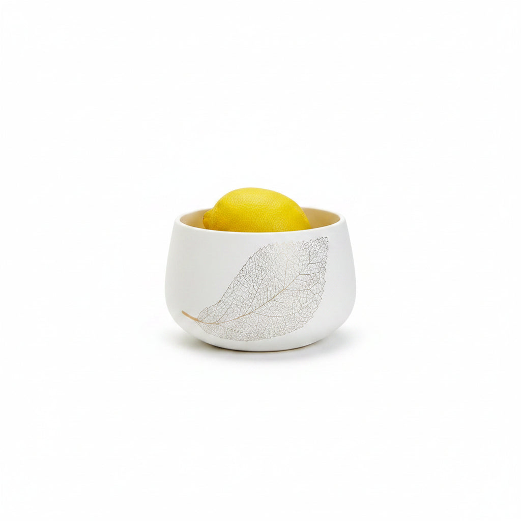 A small white ceramic bowl with a gray leaf pattern, filled with lemons on a clean white background.