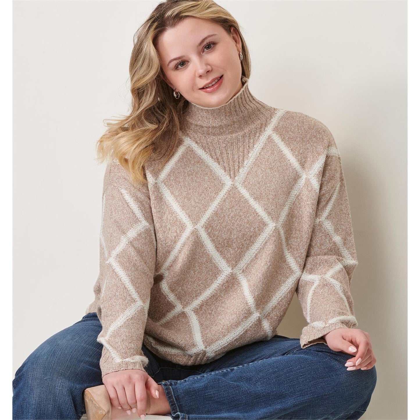 Woman wearing a beige and white patterned Charlie Paige Diamond Knit Taupe sweater sitting on a chair.