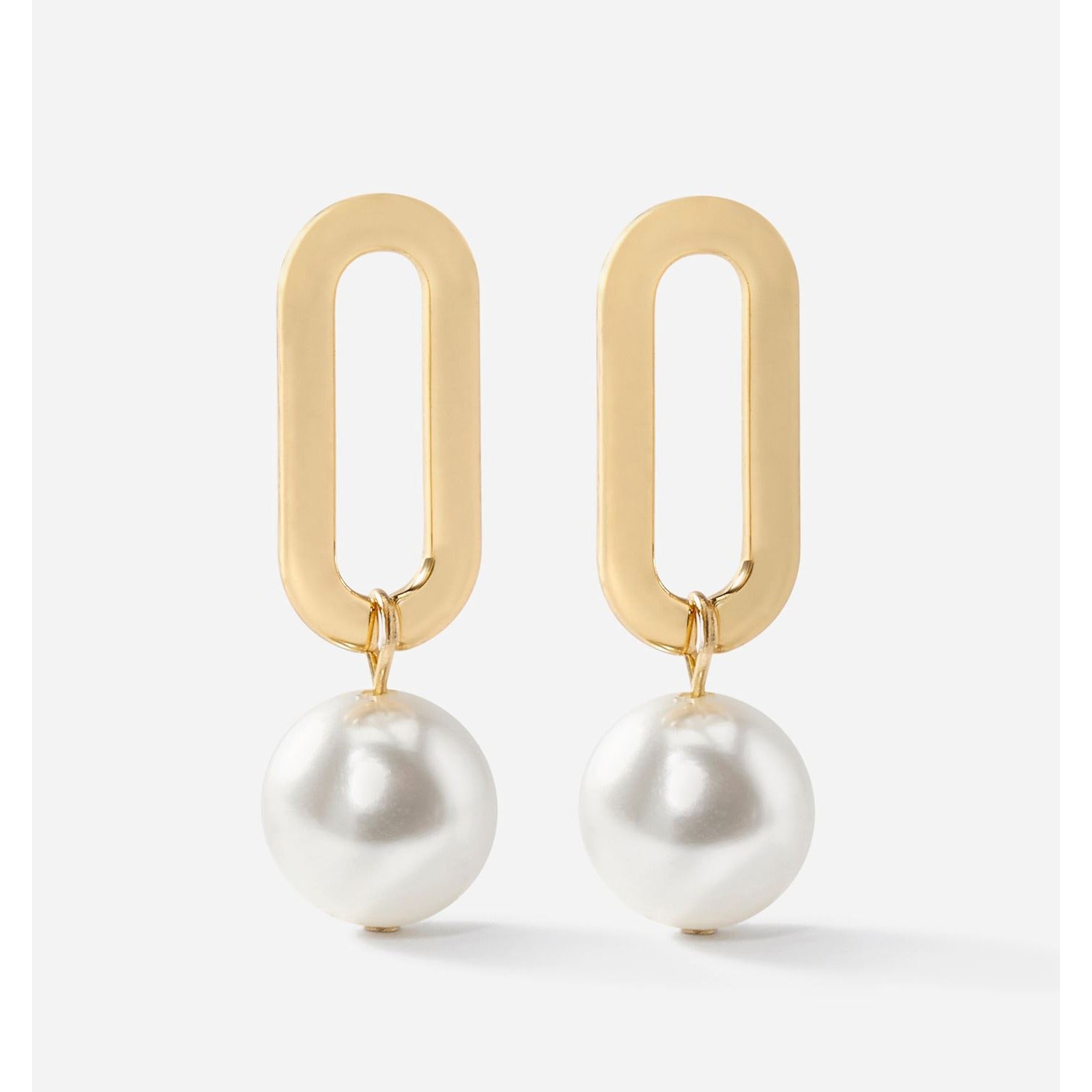 Gold oval droplet earrings with white pearls on a light gray background by Charlie Paige