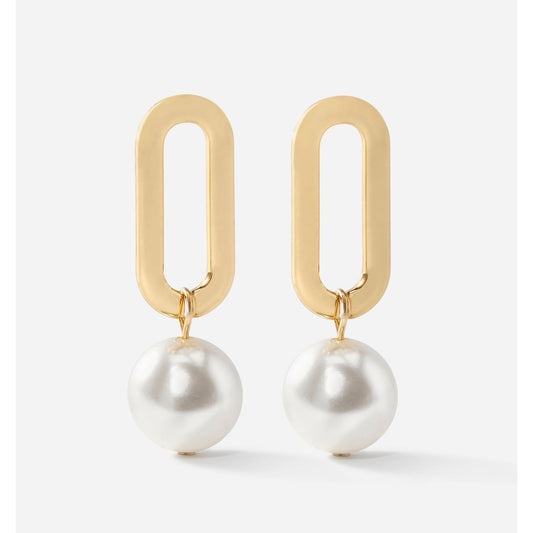 Gold oval droplet earrings with white pearls on a light gray background by Charlie Paige