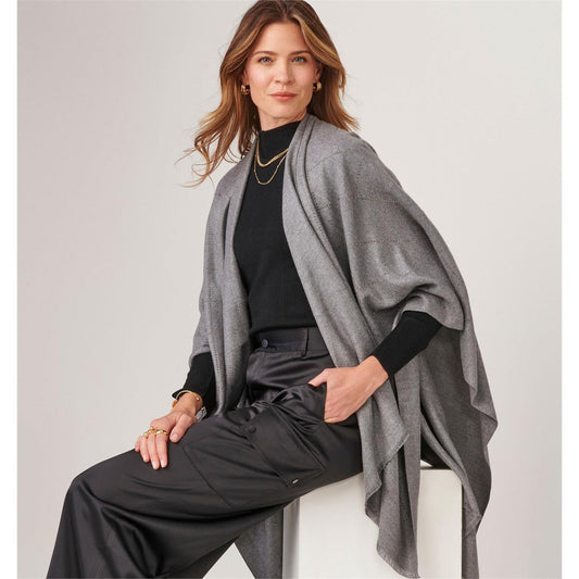 Woman wearing a Charlie Paige Sparkle Glam Wrap, Light Grey poncho over a black outfit on a light gray background