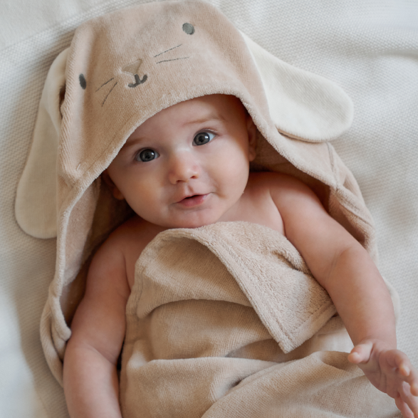 Baby wrapped in an elegant baby taupe towel with bunny ears on a soft surface