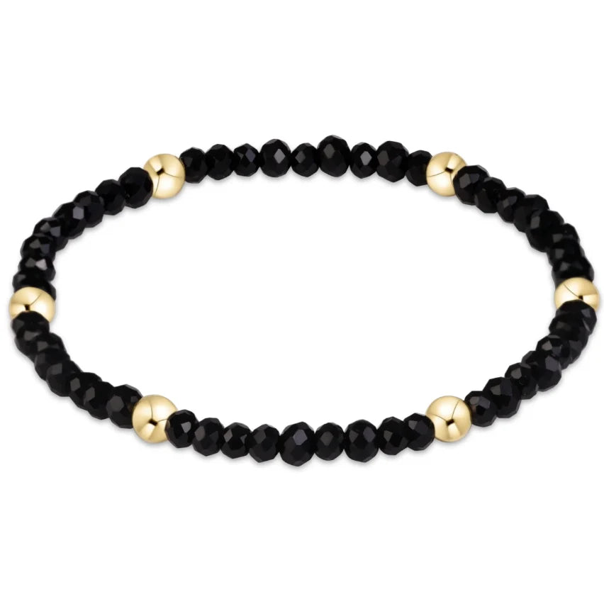 A beaded enewwton gameday flirty presence stretch bracelet featuring faceted black beads and polished gold spacer beads, displayed on a clean white background.