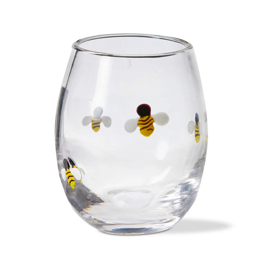 A clear stemless wine glass with a hand-applied glass bead bee icon design.